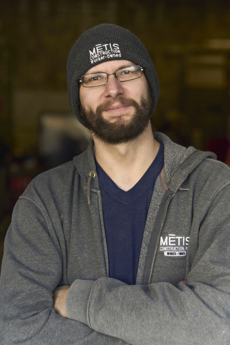 Bearded man with glasses wearing a METIS Construction beanie and gray hoodie, arms crossed, looking at the camera.