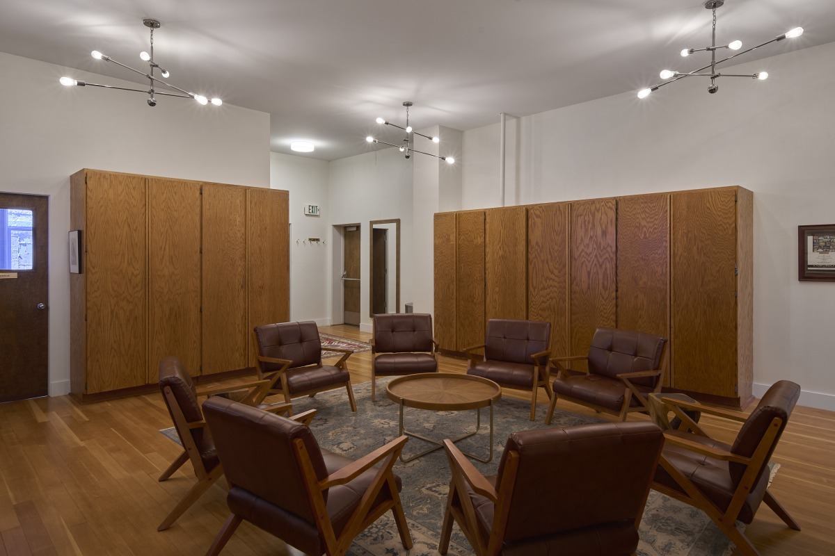 20260425_Metis_StPaul_4226 Mid-century leather chairs arranged in a circle around a round wood coffee table in a room with tall wooden storage lockers along the walls.