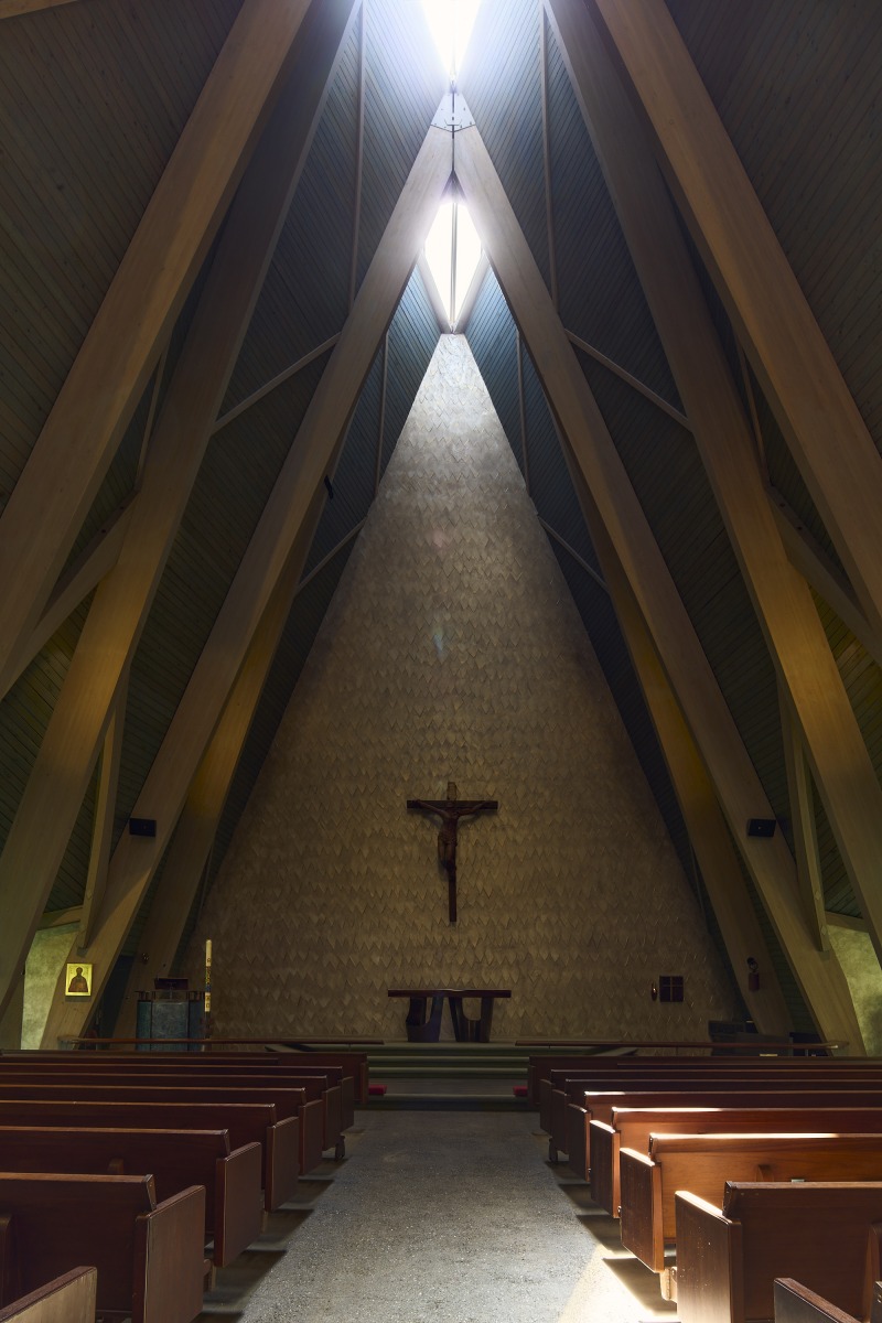 20260425_Metis_StPaul_4230 Interior of a church with a tall triangular wall, crucifix at the center, and wooden pews leading to the altar.